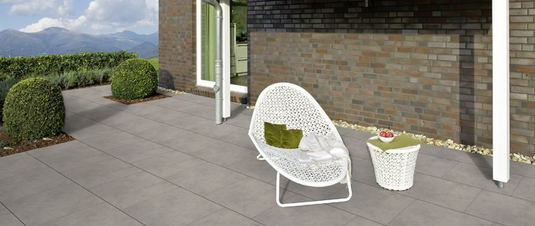 Moderne Terrasse mit großen grauen Fliesen, weißem Loungesessel, Beistelltisch und Blick auf die Berge.