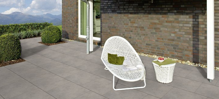 Moderne Terrasse mit großen grauen Fliesen, weißem Loungesessel, Beistelltisch und Blick auf die Berge.