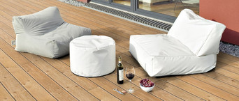 Holzterrasse mit bequemen Sitzsäcken, weißem Pouf und stilvoll arrangiertem Wein und Snacks.
