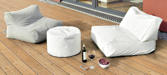 Holzterrasse mit bequemen Sitzsäcken, weißem Pouf und stilvoll arrangiertem Wein und Snacks.