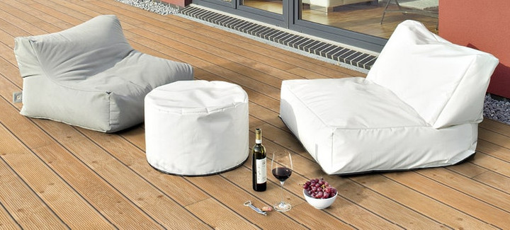 Helle Holzterrasse neben einem Gebäude mit zwei Sitzkissen und dekorativen Elementen.