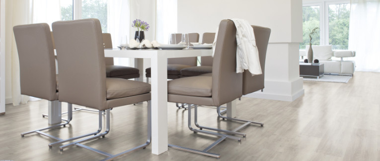 Der Boden im Esszimmer ist mit hellem Vinyl belegt. Dazu gibt es einen großen Esstisch und passende Stühle.