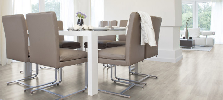 Der Boden im Esszimmer ist mit hellem Vinyl belegt. Dazu gibt es einen großen Esstisch und passende Stühle.