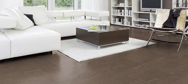 Der Boden im Wohnzimmer ist mit schokoladenfarbenem Kork ausgelegt. Weiter hinten stehen ein Sofa, ein Couchtisch und ein Sessel.