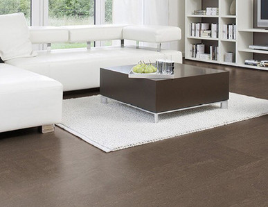 Der Boden im Wohnzimmer ist mit schokoladenfarbenem Kork ausgelegt. Weiter hinten stehen ein Sofa, ein Couchtisch und ein Sessel.