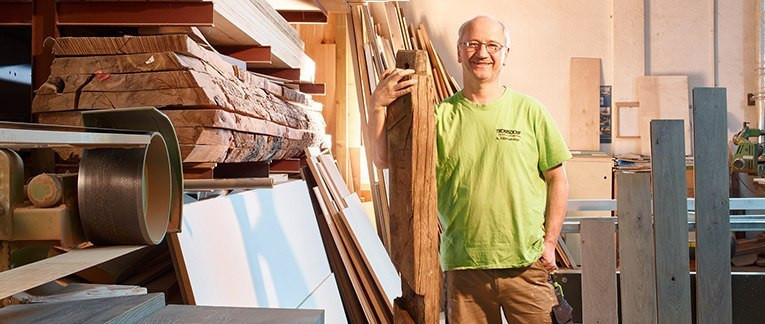Schreiner von Holzland Tromsdorf in seiner Werkstatt, umgeben von Schnittholz und Maschinen.