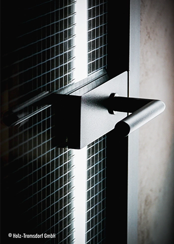 Schwarzer Türgriff an gläserner Tür mit Drahtmuster und Licht.