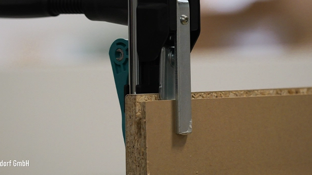 Handgeführte Zwinge fixiert eine Spanplatte, vorbereitet für Kantenbearbeitung in der Tischlerei.