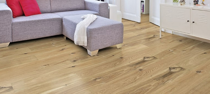 Im Wohnzimmer ist Parkett in Langdielen-Optik verlegt. Dazu passt ein Ecksofa mit bunten Kissen.