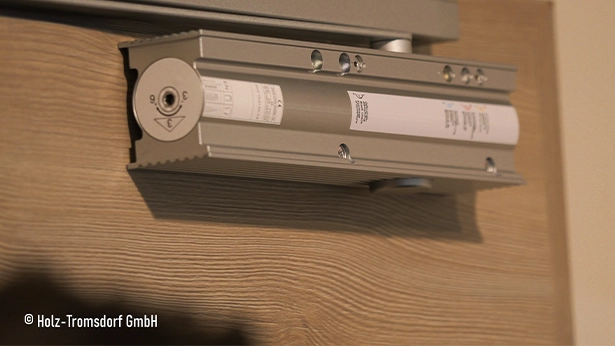 Hydraulischer Türschließer montiert an einer Holztür mit Holzmaserung.