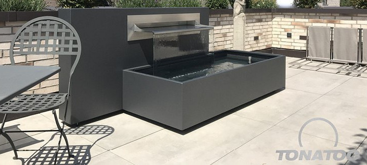 Anthrazitfarbendes Design-Wasserbecken auf einer hellen Steinterrasse