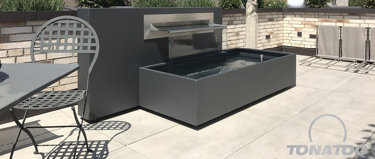Anthrazitfarbendes Design-Wasserbecken auf einer hellen Steinterrasse