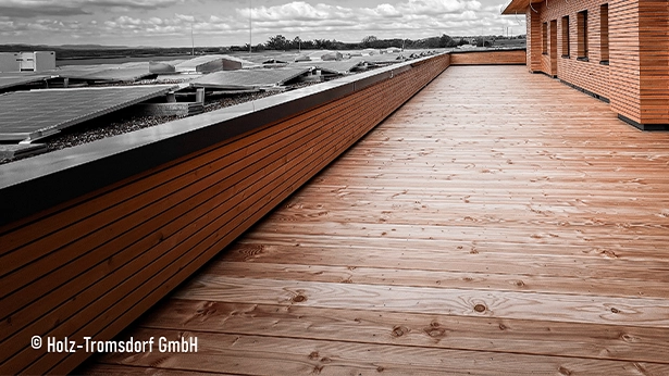 Weite Dachterrasse mit naturfarbenen Holzbohlen, Holzverkleidung an der Fassade und wolkigem Himmel.