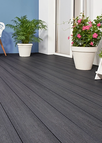 Terrasse mit dunkelgrauen Dielen, weißen Pflanzkübeln und moderner Sitzgruppe.