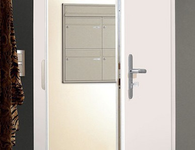 Eine halb geöffnete weiße Haustür gibt den Blick auf den Hausflur mit Briefkästen frei.