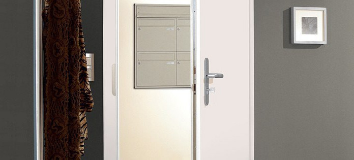 Eine halb geöffnete weiße Haustür gibt den Blick auf den Hausflur mit Briefkästen frei.