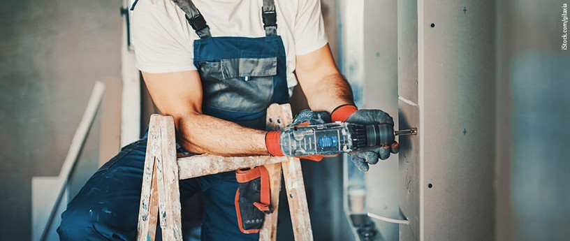 Handwerker der Gipsplatten mit einer Bohrmaschine und Schraubendreheraufsatz über einer Wand montiert.