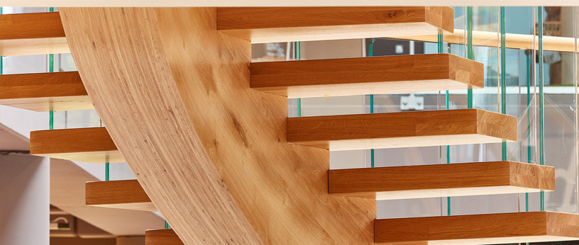 Moderne freitragende Treppe aus massivem Eichenholz mit gebogener Wangenkonstruktion und Glasgeländer.