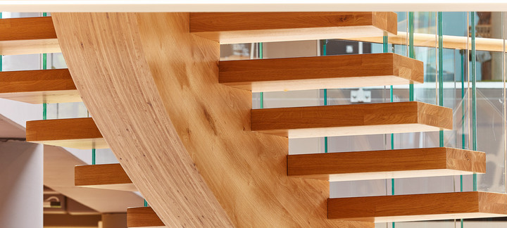 Moderne freitragende Treppe aus massivem Eichenholz mit gebogener Wangenkonstruktion und Glasgeländer.