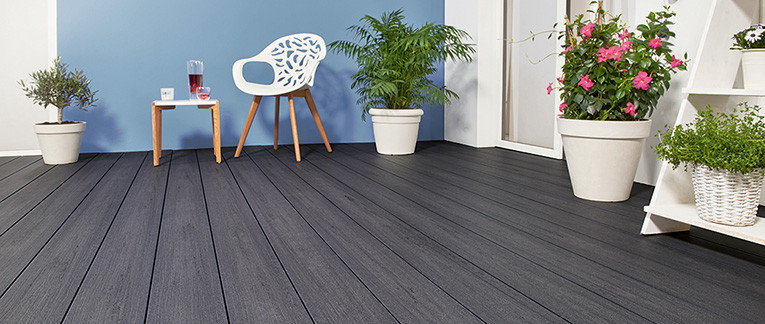 Terrasse mit dunkelgrauen Dielen, weißen Pflanzkübeln und moderner Sitzgruppe.