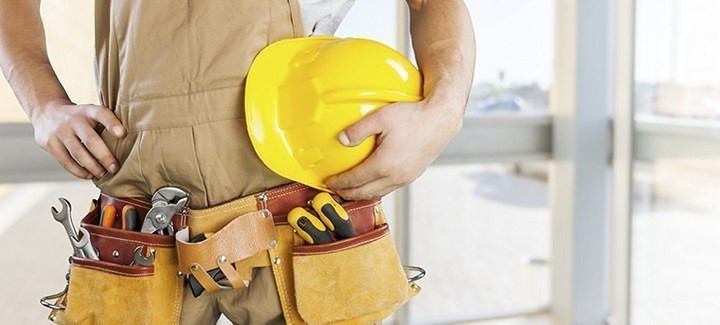 Handwerker mit gelbem Schutzhelm und Werkzeuggürtel, bereit für den Einsatz auf der Baustelle.