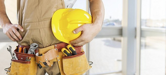 Handwerker mit gelbem Schutzhelm und Werkzeuggürtel, bereit für den Einsatz auf der Baustelle.