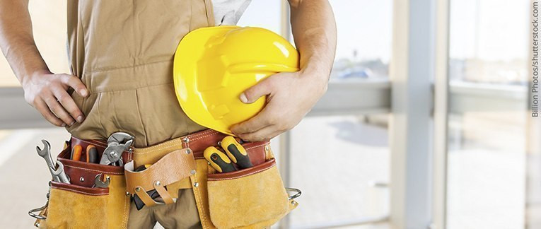 Handwerker mit gelbem Schutzhelm und Werkzeuggürtel, bereit für den Einsatz auf der Baustelle.