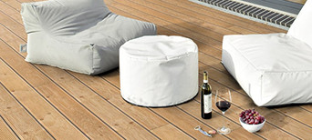 Holzterrasse mit bequemen Sitzsäcken, weißem Pouf und stilvoll arrangiertem Wein und Snacks.