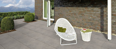 Moderne Terrasse mit großen grauen Fliesen, weißem Loungesessel, Beistelltisch und Blick auf die Berge.