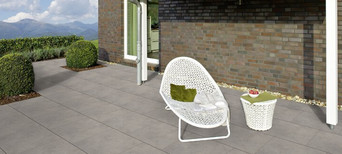 Moderne Terrasse mit großen grauen Fliesen, weißem Loungesessel, Beistelltisch und Blick auf die Berge.